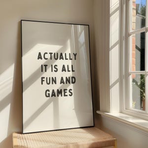 May include: A black framed print with the text "Actually it is all fun and games" in white on a white background.
