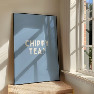May include: A framed print with a light blue background and white text that reads "Chippy Tea?" The print is hanging on a wall with a window to the right.