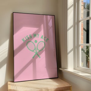 Könnte beinhalten: Ein rosa gerahmtes Poster mit dem Text "Kiss My Ace" in grüner Schrift. Zwei grüne Tennisschläger sind in der Mitte des Posters mit einem grünen Tennisball gekreuzt.