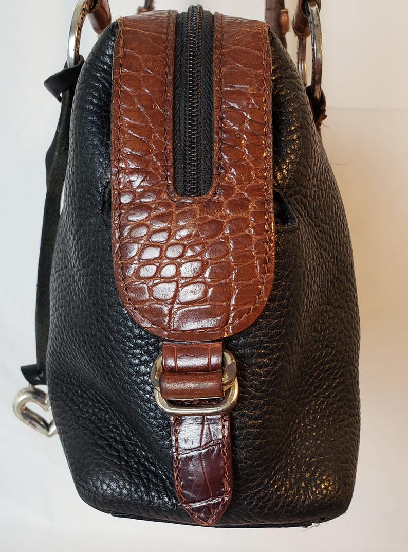 Puede incluir: Bolso de mano de cuero negro con detalles marrones con textura de cocodrilo. El bolso tiene una cremallera superior, un cierre de hebilla y herrajes plateados. El dise&ntilde;o combina cuero liso y texturizado.