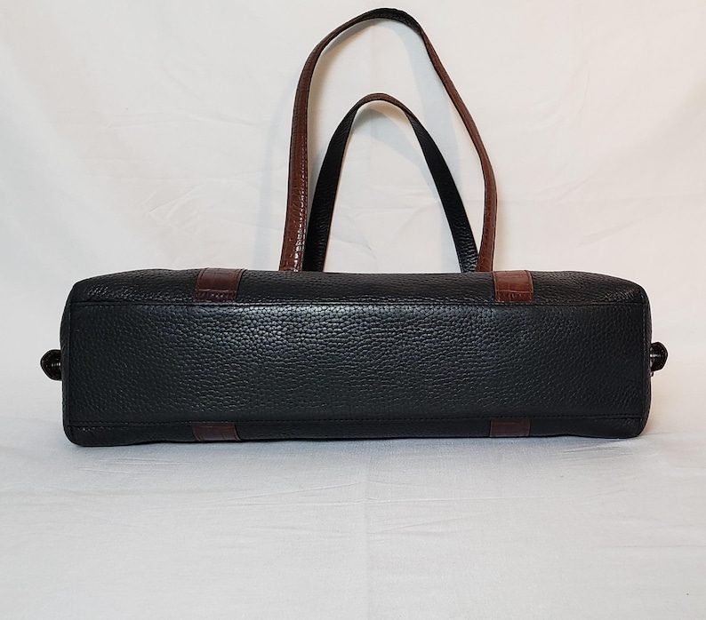 Puede incluir: Bolso tote de cuero negro con detalles y asas marrones. El bolso presenta un exterior texturizado y una forma rectangular. Las asas son marrones y el bolso tiene detalles marrones en los laterales. Dise&ntilde;ado para transportar art&iacute;culos.