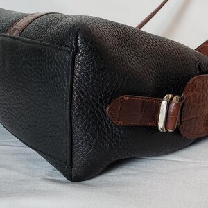 Puede incluir: Bolso de mano de cuero negro con detalles de cuero marr&oacute;n con relieve de cocodrilo. El bolso tiene forma rectangular con una superficie texturizada y una hebilla plateada. Con correa para el hombro.
