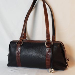 Puede incluir: Bolso de mano de cuero negro con detalles y asas en relieve de cocodrilo marr&oacute;n. El bolso presenta herrajes plateados y un charm en forma de coraz&oacute;n. El bolso tiene forma rectangular.