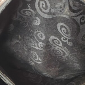 Puede incluir: Vista interior de un bolso marr&oacute;n con forro estampado. El forro presenta un dise&ntilde;o de remolino repetido en un tono m&aacute;s oscuro, creando un contraste sutil. El interior del bolso es visible, mostrando la textura y el dise&ntilde;o de la tela.