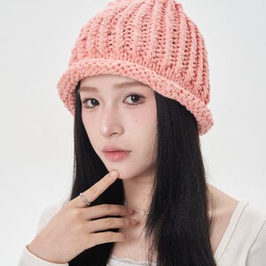 May include: A pink knitted beanie with a wide brim. The beanie is made of a soft, chunky yarn and has a simple, classic design.