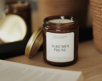 May include: A brown glass candle jar with a gold lid. The candle is labeled "Douce Flamme" and "Agrumes Prune". The candle is made in France and has a soy wax base.