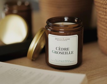 May include: A brown glass candle jar with a gold lid. The candle is labeled "DOUCE FLAMME" and "CÈDRE GROSELLE". The label also says "FAIT MAIN EN FRANCE" and "SOJA | PARFUMS DE Grasse".