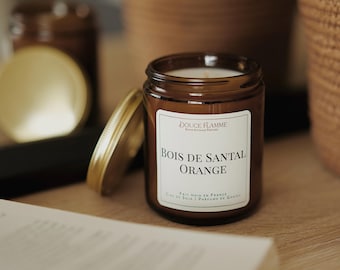 May include: A brown glass candle jar with a gold lid. The candle is labeled "Bois de Santal Orange" and "Douce Flamme". The candle is made with soy wax and is hand-poured in France.
