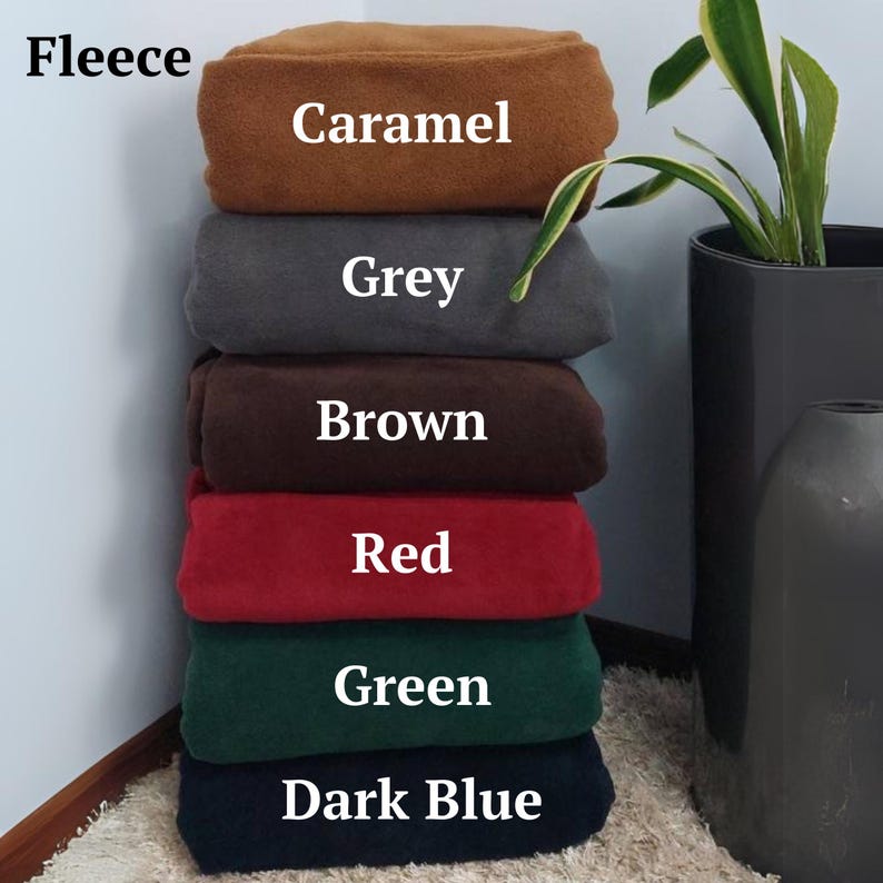 May include: A stack of six fleece blankets in different colours: caramel, grey, brown, red, green, and dark blue. The text "Fleece" is visible at the top of the image.