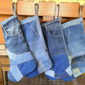 May include: Four holiday stockings crafted from repurposed blue denim jeans, each featuring a unique patchwork design with visible pockets, belt loops, and varying shades of blue fabric. Each stocking includes a denim loop for hanging purposes.