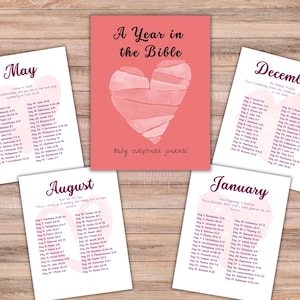 Puede incluir: Un diario de escritura bíblica diaria "A Year in the Bible" con un diseño de corazón rosa acuarela. Incluye páginas mensuales con lecturas diarias de las Escrituras para enero, mayo, agosto y diciembre. El diario está sobre una superficie de madera.