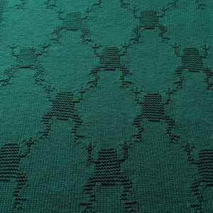 May include: A green knitted blanket with a pattern of frogs. The blanket is made with a soft, textured yarn and has a fringed edge.