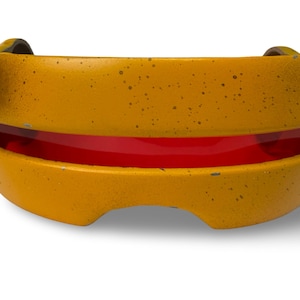 May include: A yellow, curved object with a red interior. The exterior has a textured, speckled appearance. Two small, curved handles are on the top. The object is likely made of metal or a similar material.
