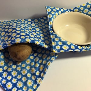 May include: Two blue and white floral fabric bowl cozies. One cozy is holding a white bowl and the other is holding a brown potato.
