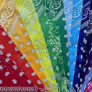 May include: A collection of colorful bandanas arranged in a rainbow spectrum. Each bandana features a paisley design with white accents. The colors range from red, orange, yellow, green, blue, and purple.