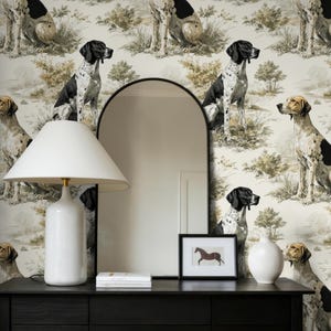 以下が含まれることがあります： 白いランプ、鏡、額入りのアートワークを備えた黒いコンソールテーブル。背景には犬の模様の壁紙があります。テーブルの下には、毛布が入った籐のバスケットがあります。