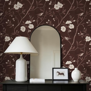 May include: A black console table with a white lamp, mirror, and framed horse art. A white vase and a stack of books sit on the table. The background is a floral wallpaper with white flowers and birds. A wicker basket with a blanket is below the table.