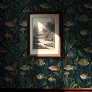 May include: A framed black and white landscape print featuring a river and trees, mounted on a dark wallpaper background with a repeating pattern of various fish, aquatic plants, and coral in shades of green, blue, and muted gold tones.