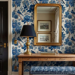 May include: A hallway with blue floral wallpaper, a wooden table, and a gold-framed mirror. A black lamp with a navy shade sits on the table. A blue floral bench is in front of the table. The wallpaper features blue flowers and birds.