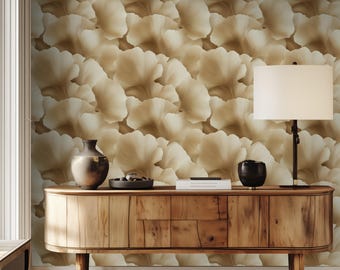 Op de afbeelding: Een houten consoletafel met een lichtbruine afwerking. De tafel heeft een gebogen voorzijde en drie poten. De tafel staat voor een muur met een behang met een patroon van overlappende beige bloemblaadjes.