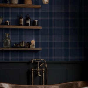 May include: A copper freestanding bathtub with a dark gray towel draped over the edge, positioned below a brass faucet. Three wooden shelves hold glass bottles, candles, and a small plant against a dark blue plaid wallpaper background.
