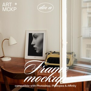 May include: A framed black and white portrait of a woman's profile sits on a wooden desk. A vintage typewriter and a white desk lamp with a gold arm are also on the desk. The words "Frame mockup" are written in cursive.