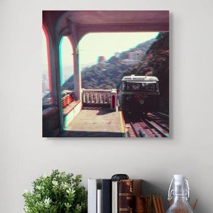 Könnte beinhalten: Ein gerahmter Leinwanddruck eines Straßenbahnwagens auf Gleisen, gesehen von einer überdachten Plattform. Das Bild hat einen 3D-Effekt mit roten und blauen Farbverzerrungen. Der Druck wird über einem Holztisch mit Kopfhörern, Büchern und einer Wasserflasche angezeigt.