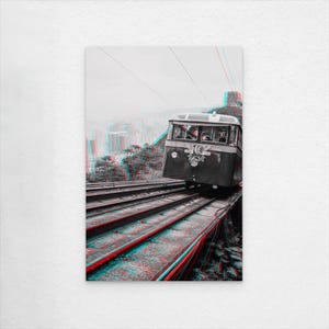 Könnte beinhalten: Schwarz-Weiß-Druck eines Standseilbahnzugs, der eine Strecke hinauffährt, mit 3D-Effekt. Der Triebwagen hat ein Logo auf der Vorderseite. Die Gleise sind rot und blau, und der Hintergrund zeigt eine Stadt und Berge.
