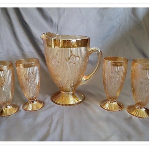 May include: A vintage glassware set featuring a pitcher and four matching glasses. The set has a textured, amber-colored glass with floral and vertical line designs. The rims and bases have a gold trim, creating an elegant aesthetic.