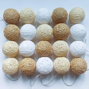 Pode incluir: Uma corrente de vinte coberturas esféricas para luzes dispostas numa grelha de quatro por cinco. Cada esfera é construída com fio enrolado em tons alternados de branco, creme e castanho claro, criando uma aparência texturizada.