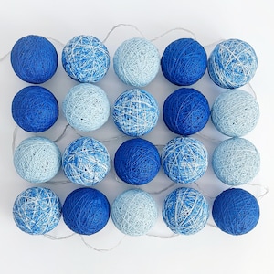 May include: A string of 20 blue cotton ball lights in varying shades of blue. The lights are arranged in a grid pattern and connected by a thin silver wire. The cotton balls have a textured, woven appearance.