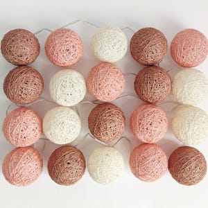Könnte beinhalten: Eine Lichterkette mit 20 Baumwollkugeln in drei Farben: Creme, Hellrosa und Hellbraun. Die Lichter sind mit einem durchsichtigen Draht verbunden.