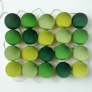 May include: A string of green cotton ball lights in various shades, from dark to light. The lights are strung on a silver wire, creating a colourful display. Ideal for adding a touch of whimsy to any space. Each ball is approximately 6 cm in diameter.