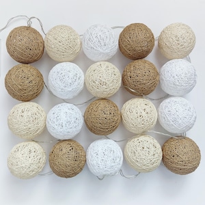 Può includere: Una stringa di luci decorative a globo. Le luci sono realizzate in spago intrecciato in vari colori neutri, tra cui bianco, beige e marrone. Le luci sono disposte a griglia e sono collegate da un sottile filo d'argento.