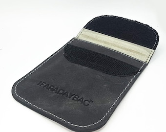 May include: A black rectangular pouch with rounded corners and white contrast stitching. The front features the embossed text FARADAYBAG. The top flap includes a black hook-and-loop fastener strip and a light-colored interior lining.