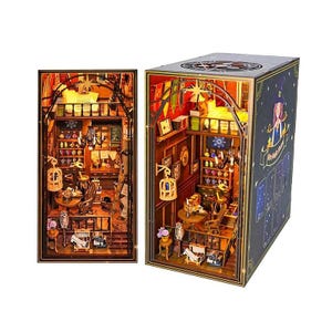 May include: A miniature diorama kit featuring a multi-level room with a loft, a chandelier, shelves filled with small bottles, a wooden table, chairs, and a hanging birdcage. The exterior box displays a graphic of a person and the text My Magic House.