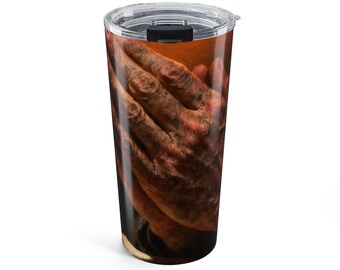 May include: A cylindrical stainless steel tumbler featuring a wrap-around graphic of weathered, textured hands pressed together in a prayer position. The design displays deep brown and earthy tones with a clear plastic lid and a black sliding closure.