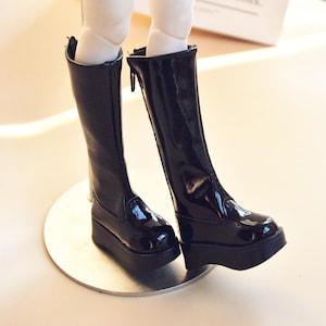 May include: A pair of black patent leather knee-high boots with a zipper on the back. The boots have a thick platform sole and a pointed toe.