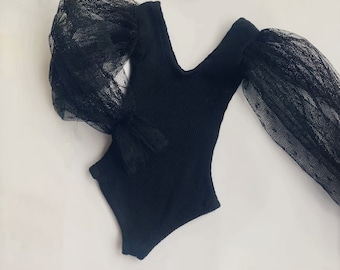 May include: Black bodysuit with long sleeves and a V-neck. The sleeves are made of sheer black mesh.