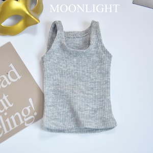 May include: A light gray ribbed tank top with a scoop neck. The text "don't feel bad about feeling!" is on a tan card. A gold and black mask are in the background. The word "MOONLIGHT" is at the top.
