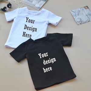 May include: Two blank t-shirts, one white and one black, with the text "Your Design Here" and "Your design here" printed on them.