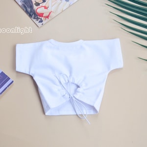 May include: White crop top with a drawstring tie at the back.