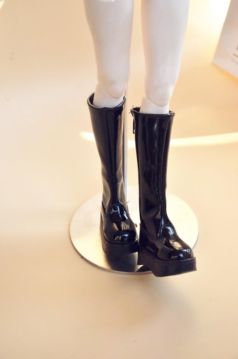 May include: A pair of black knee-high boots with a shiny finish. The boots have a zipper on the inside of each boot.