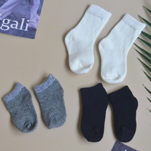 May include: Six pairs of socks in three different colours: white, grey, and black. The socks are all ankle-length and have a ribbed texture.
