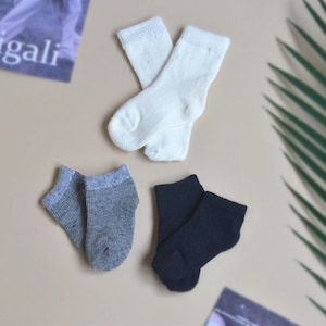 May include: Three pairs of socks in different colours: white, grey, and black. The socks are all ankle-length and made of a soft, comfortable material.