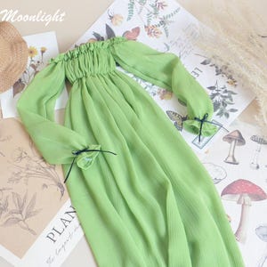 May include: A light green off-the-shoulder dress with long sleeves, a straw hat, and a small white statue. The dress has a gathered neckline and cuffs tied with black ribbons. The word "Moonlight" is in the top left corner.