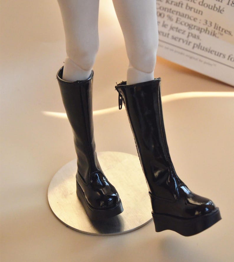 May include: A pair of black knee-high boots with a shiny finish and a thick platform sole.