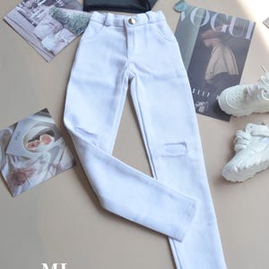 May include: White denim jeans with distressed details. The jeans have a straight leg fit and a button fly closure.