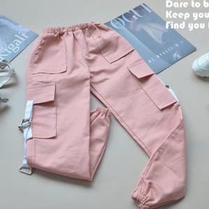Op de afbeelding: Roze cargo broek met witte banden en zakken. De broek heeft een elastische tailleband en een ontspannen pasvorm.