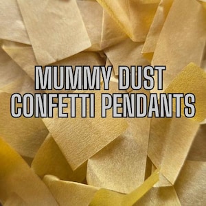 May include: Close-up of a pile of confetti pendants in shades of yellow and beige. The text "MUMMY DUST CONFETTI PENDANTS" is overlaid on the image in a bold, black-outlined font. The confetti pieces are rectangular and overlapping.